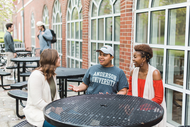 Three people talking at a table outside the Olt Student Center at Anderson University