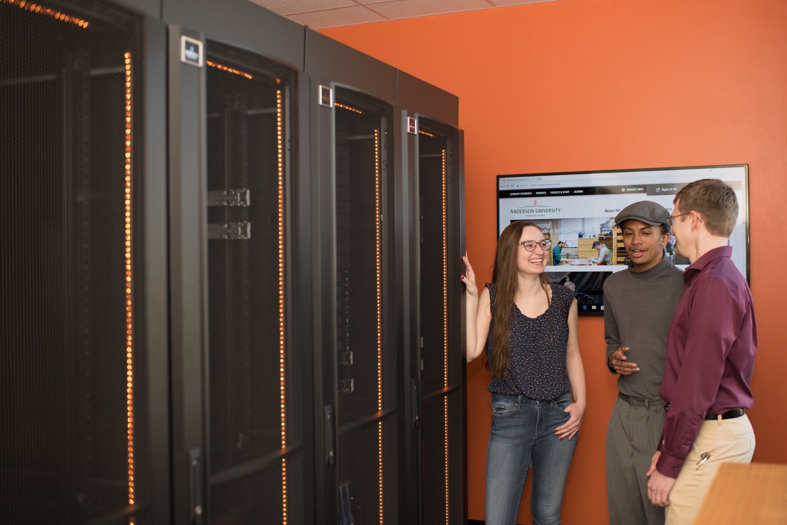 Three students stand among the servers in the Cybersecurity Engineering Lab