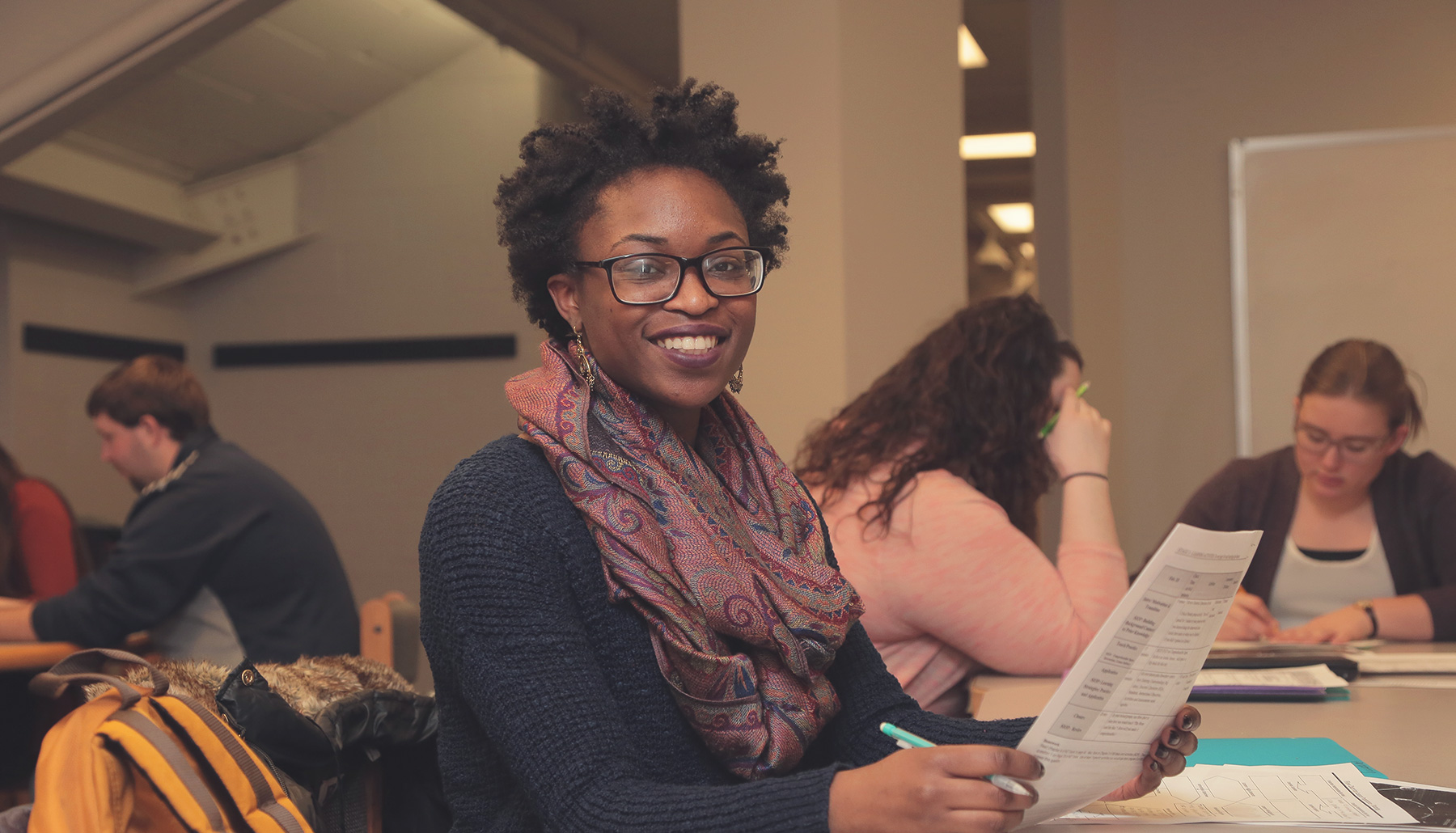 a female student smiles at the camera while holding papers