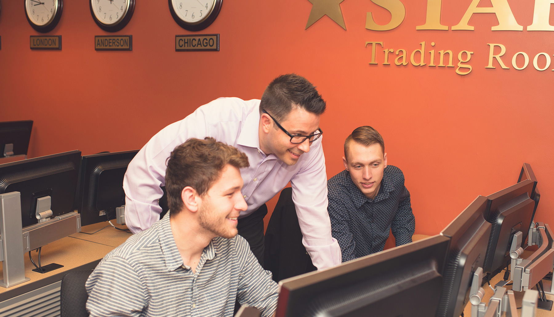 a professor works with two students in the STAR trading room