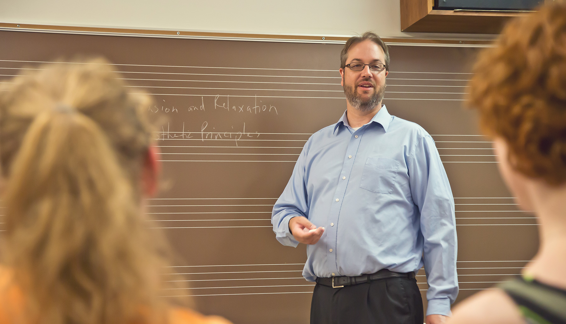 a male professor talks to a class in front of a blackboard