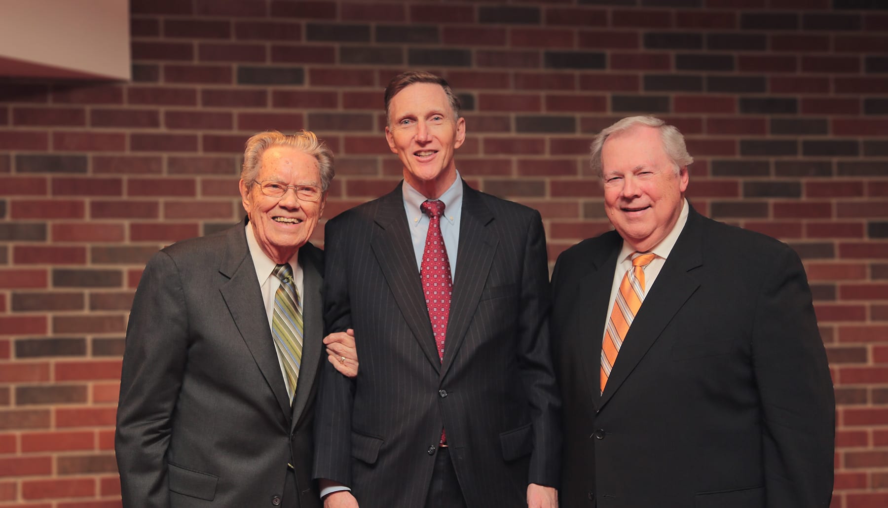 President Nicholson, Edwards, and Pistole posing for a photo with a red brick background.