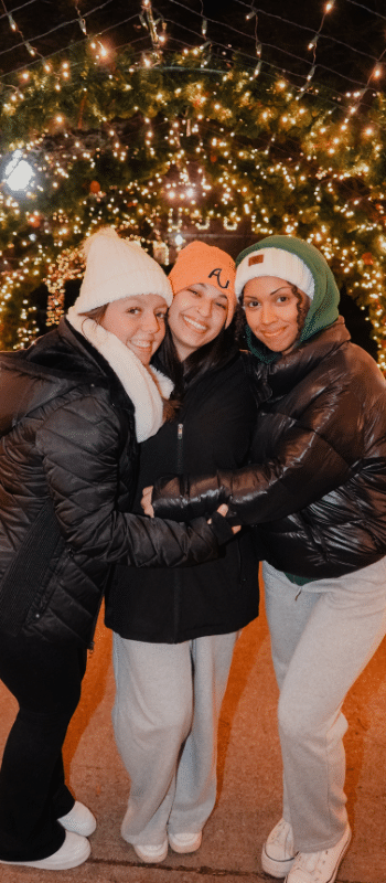 Three girls under a Christmas lights tunnel