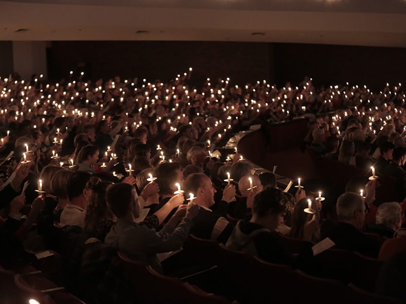 Dozens of people raising their candles during Christmas ceremony.