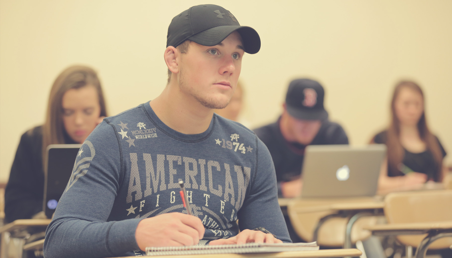 a young man with heavy stubble taking notes in class
