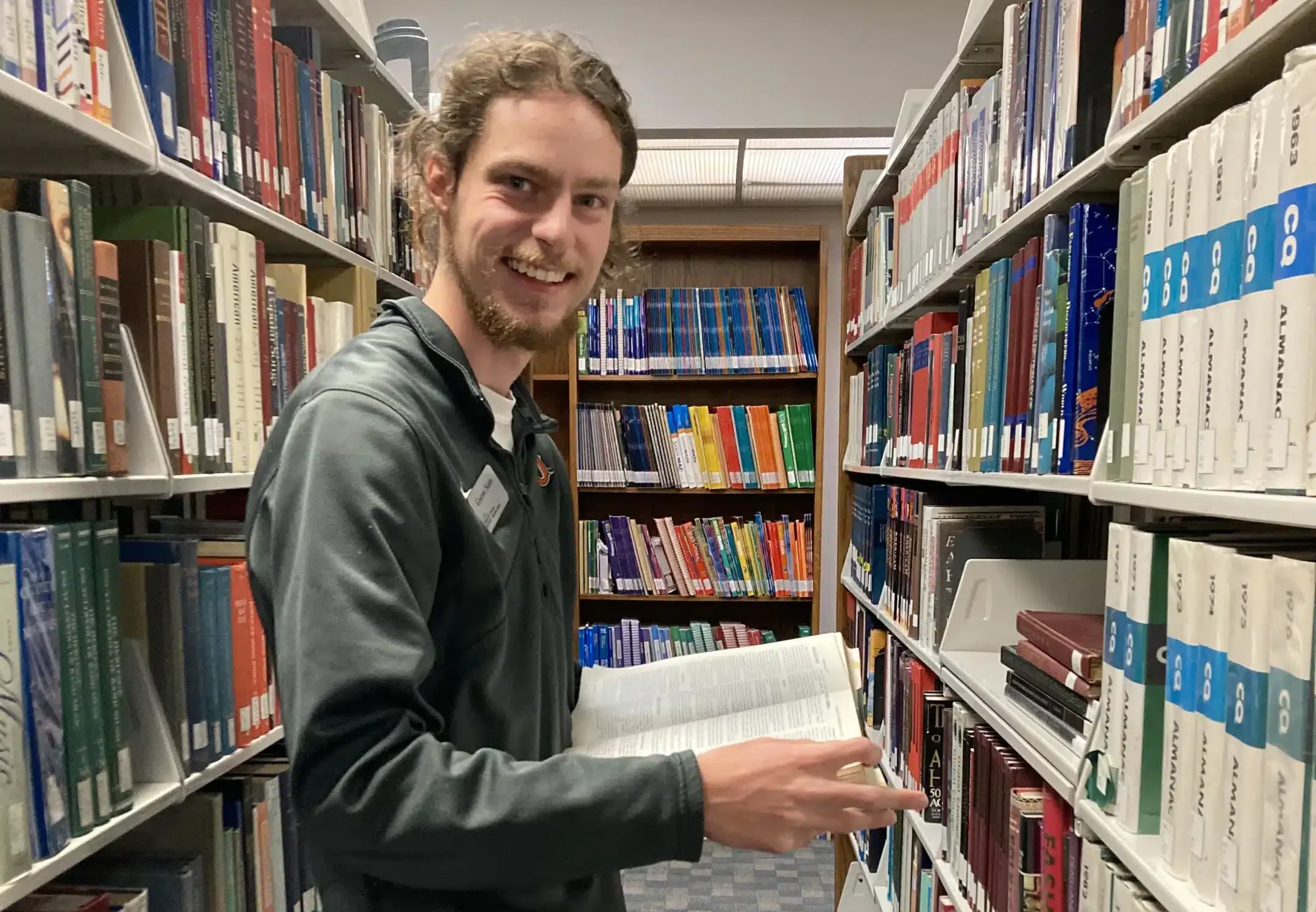 graeme_states Graeme States smiles at the camera while holding a book amidst stacks in the Nicholson Library