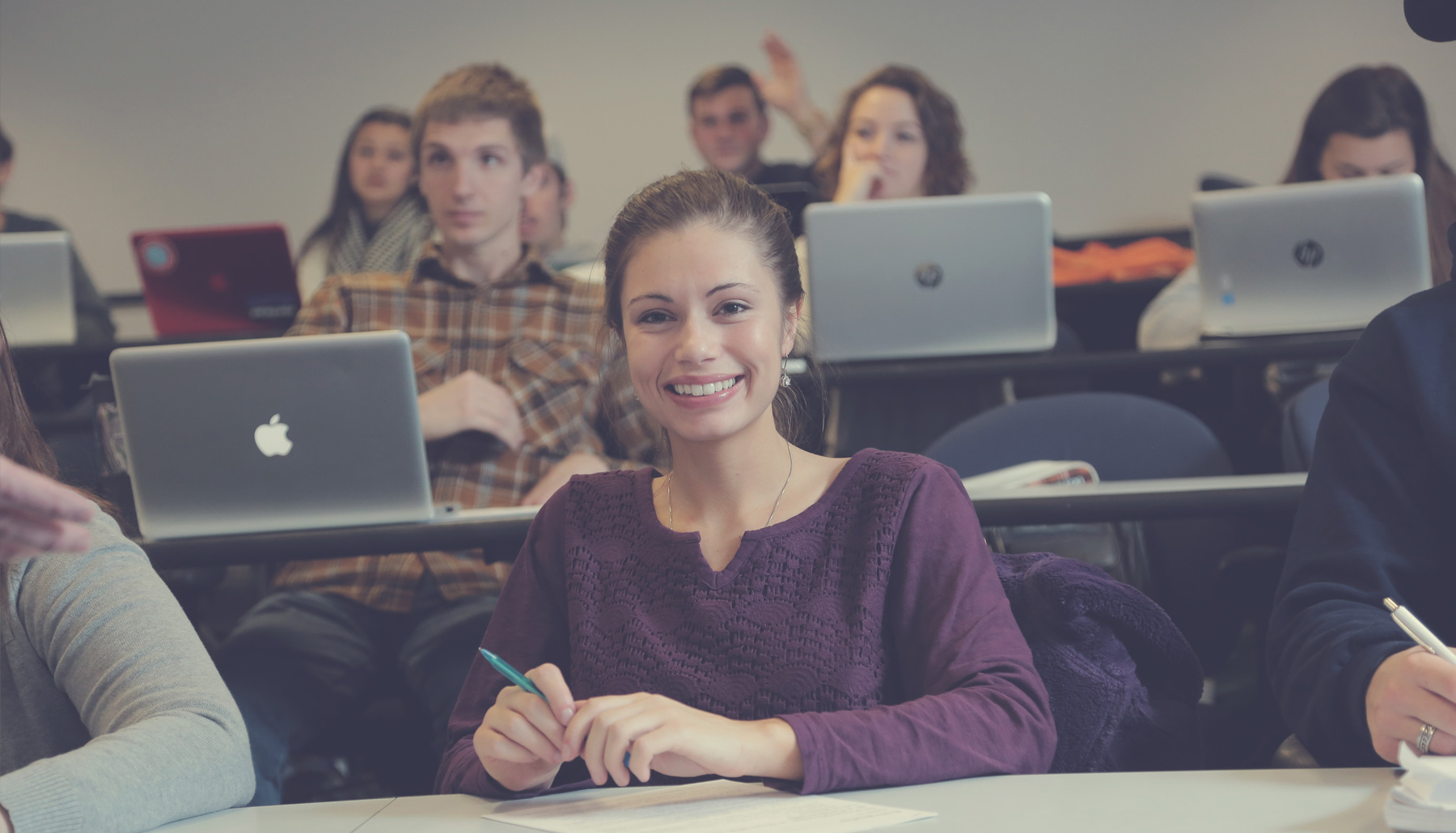 a young woman smiles at the camera in a classroom with many laptops