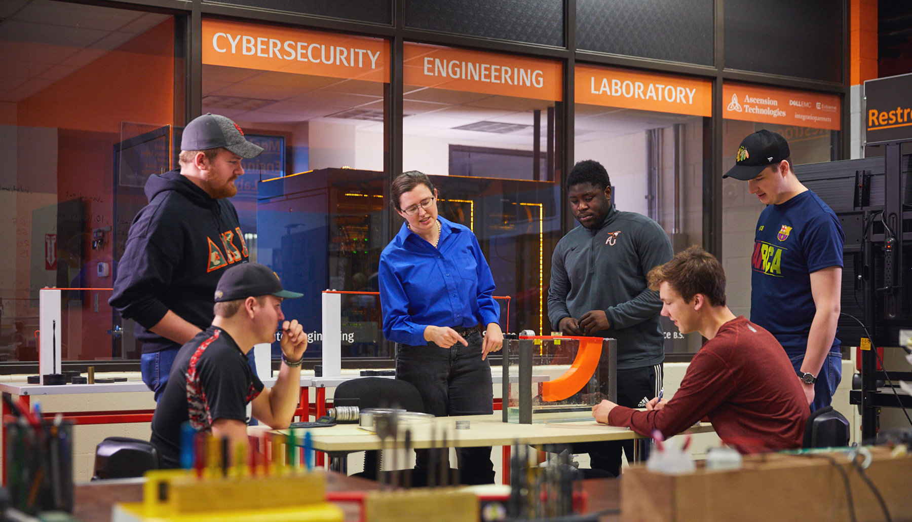Three students stand among the servers in the Cybersecurity Engineering Lab