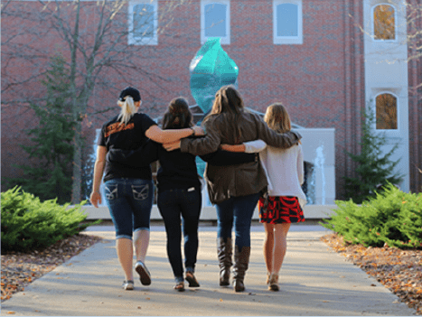 Four women walking to class arm in arm.