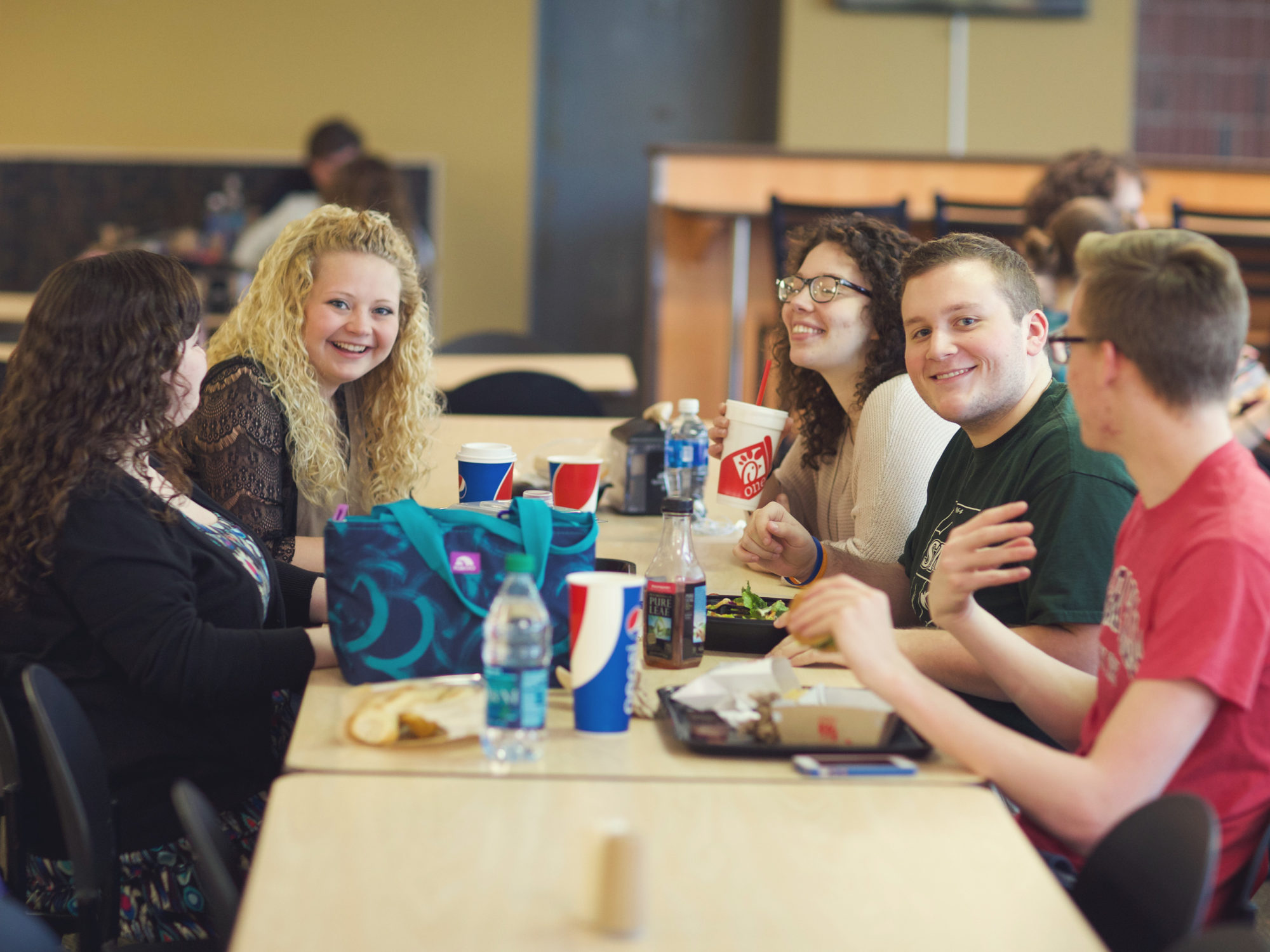 Five students gathered together at a long table eating lunch.