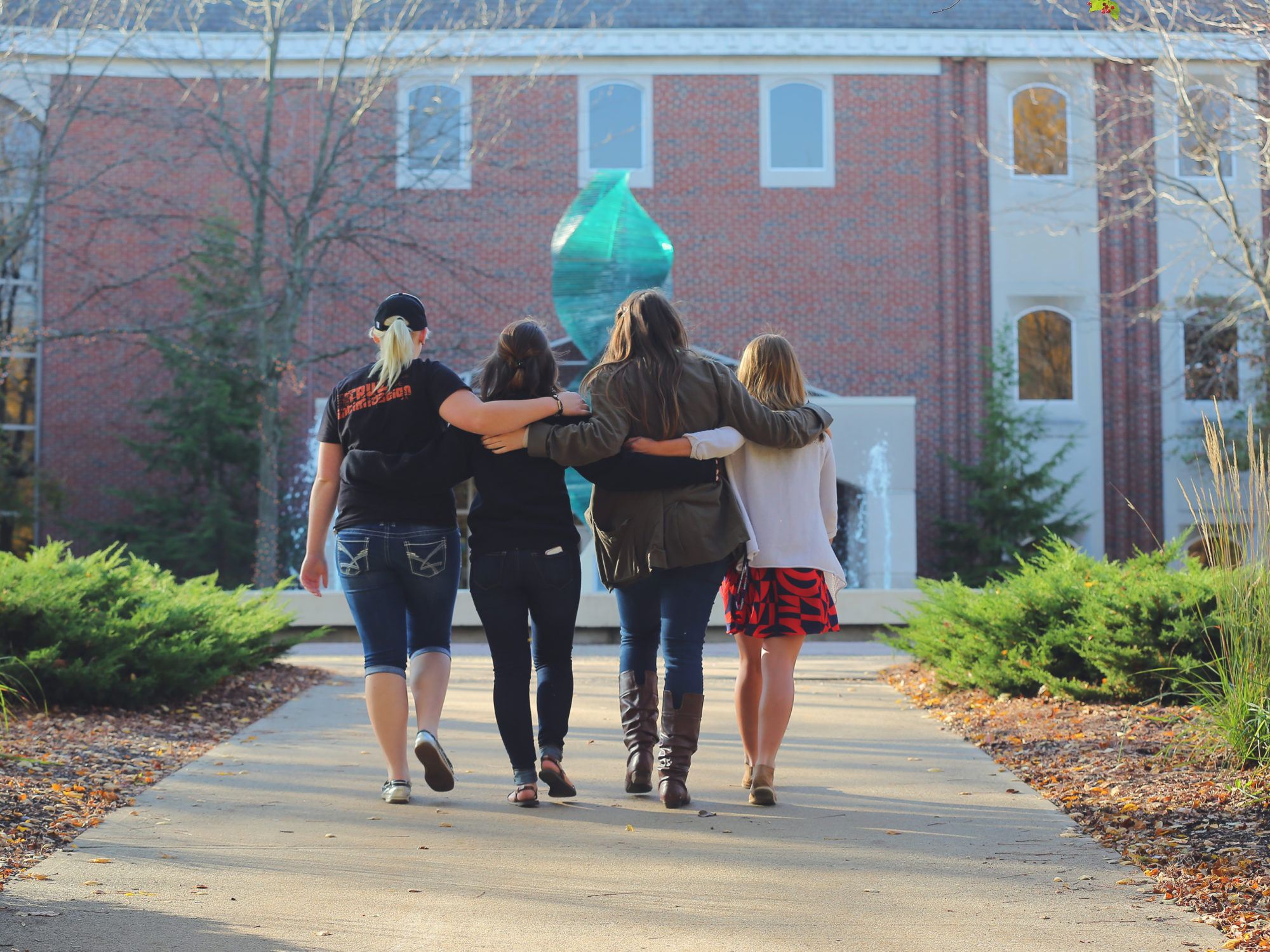 four female students with arms around each other walking to class