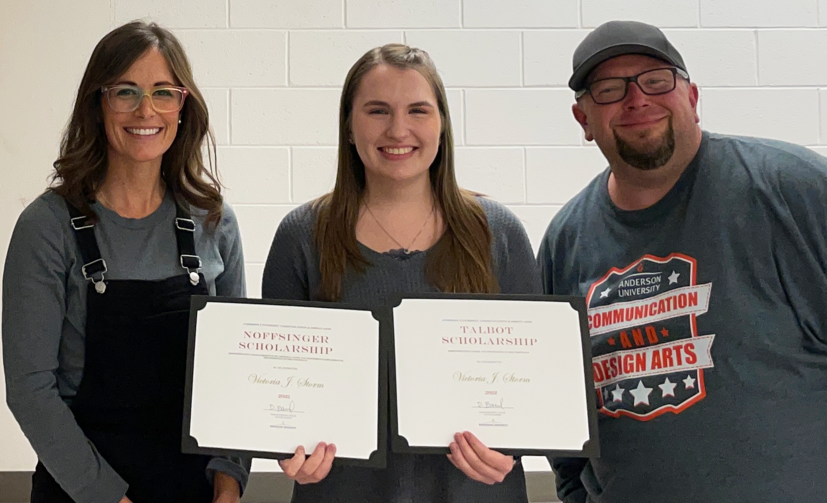 Tori Storm holding the Talbott and Noffsinger scholarships with professors Holly Sims and Jason Higgs